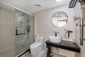 Une salle de bain moderne avec une douche à parois de verre, des toilettes blanches, un meuble-lavabo noir avec un miroir rond et un lavabo blanc.