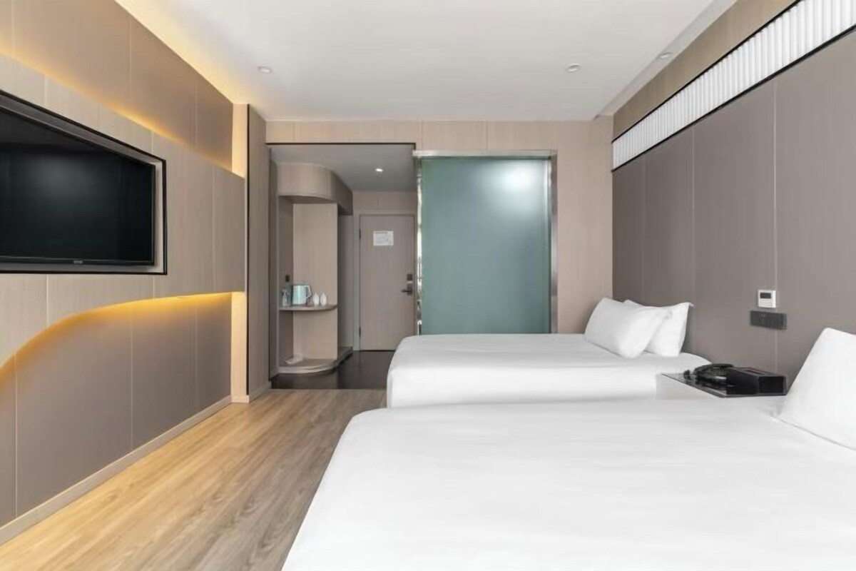 Une chambre d’hôtel moderne équipée d’un téléviseur à écran plat, de deux lits, d’une table de chevet et d’une salle de bain visible à travers une porte ouverte.