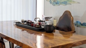 A wooden table with a tray holding various tea cups and a black pot, set against a wall with a painting. - Longgang Hongmao Film Hotel (Longgang)