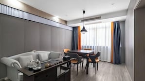 A modern hotel room with a grey sofa, a wooden coffee table, a dining table with chairs, and a large window with curtains. - Longgang Hongmao Film Hotel (Longgang)