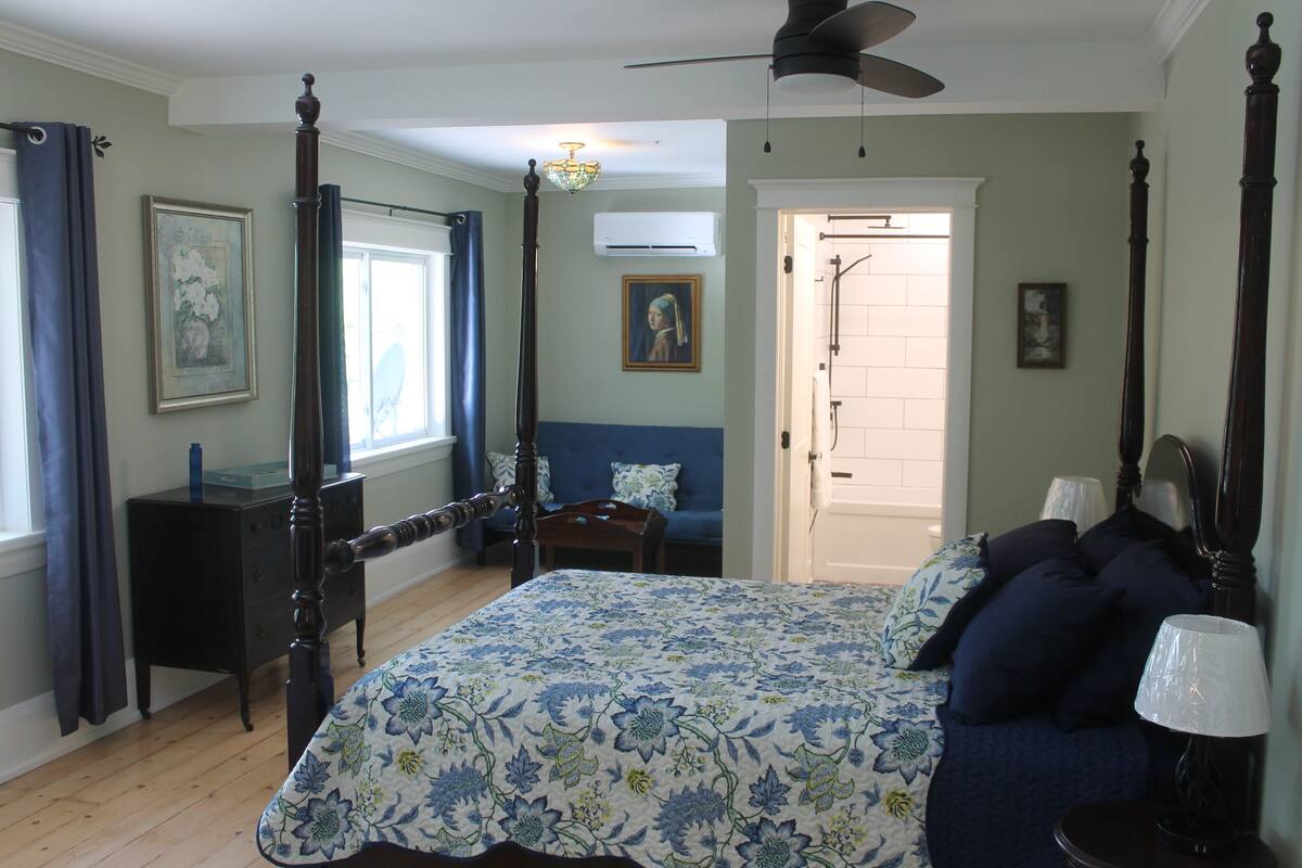 Un dormitorio con una cama con dosel, una mesita de noche, un aparador y una ventana con cortinas.
