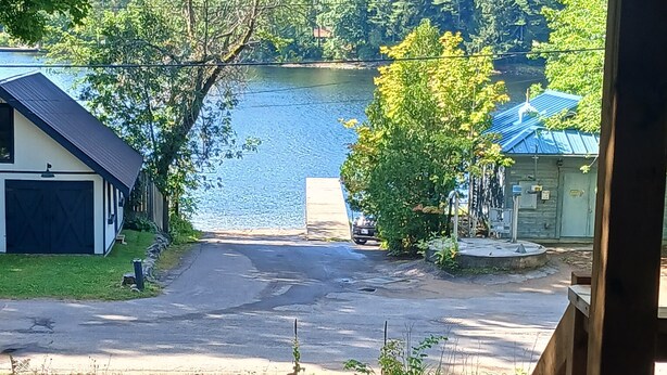 A view of a lakeside property with a paved driveway leading to a dock, surrounded by lush greenery and residential buildings. - Cranberry Moon Inn B&B (Bala)