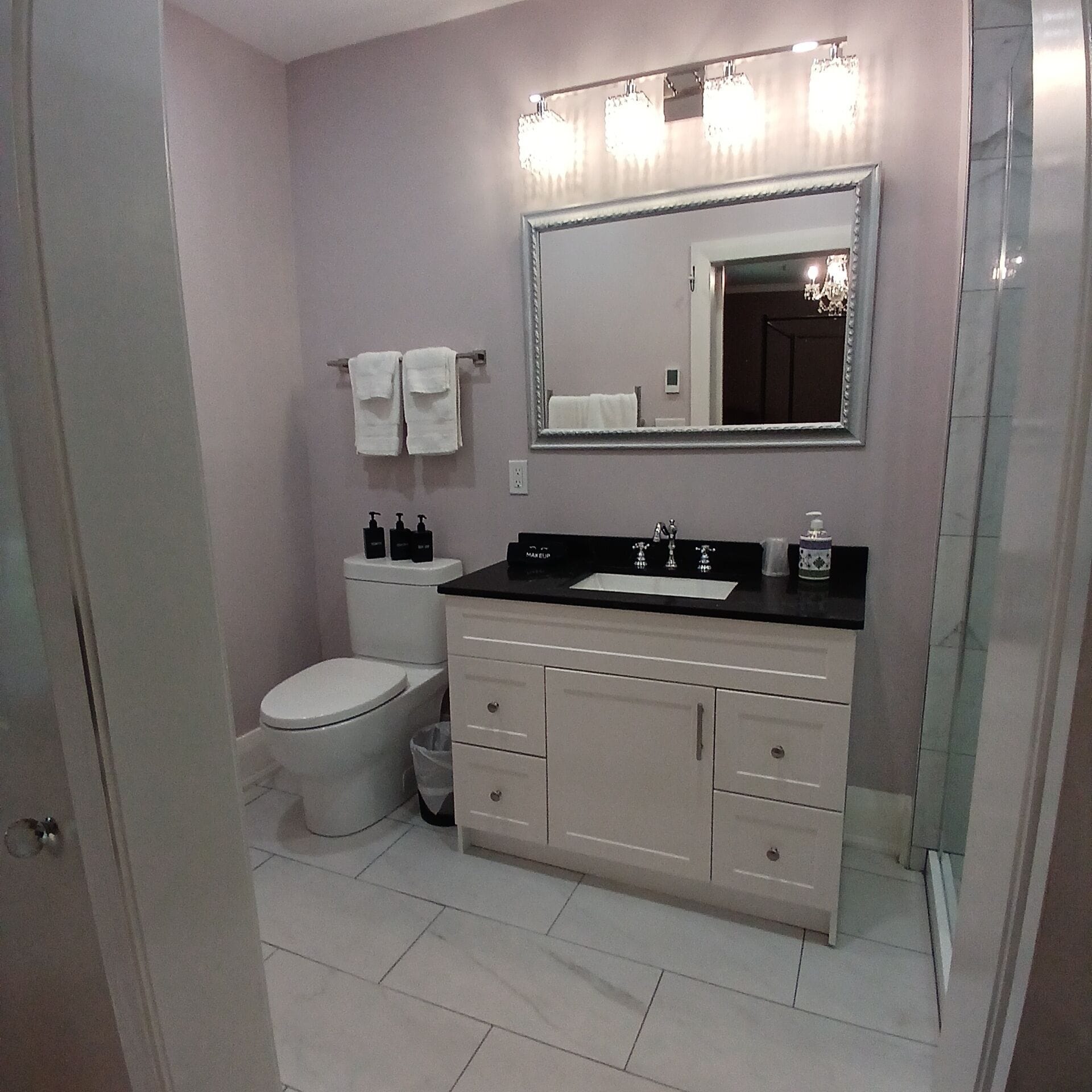 Un bagno con il water bianco, un mobile lavabo con piano nero e uno specchio con luci sopra.