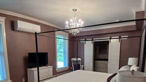 A bedroom with a four-poster bed, a chandelier, a television on a dresser, and a window with blinds. - Cranberry Moon Inn B&B (Bala)