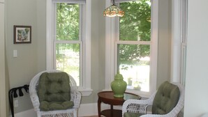A room with two white wicker chairs, a small table with a green vase, and a black rug on a wooden floor. - Cranberry Moon Inn B&B (Bala)