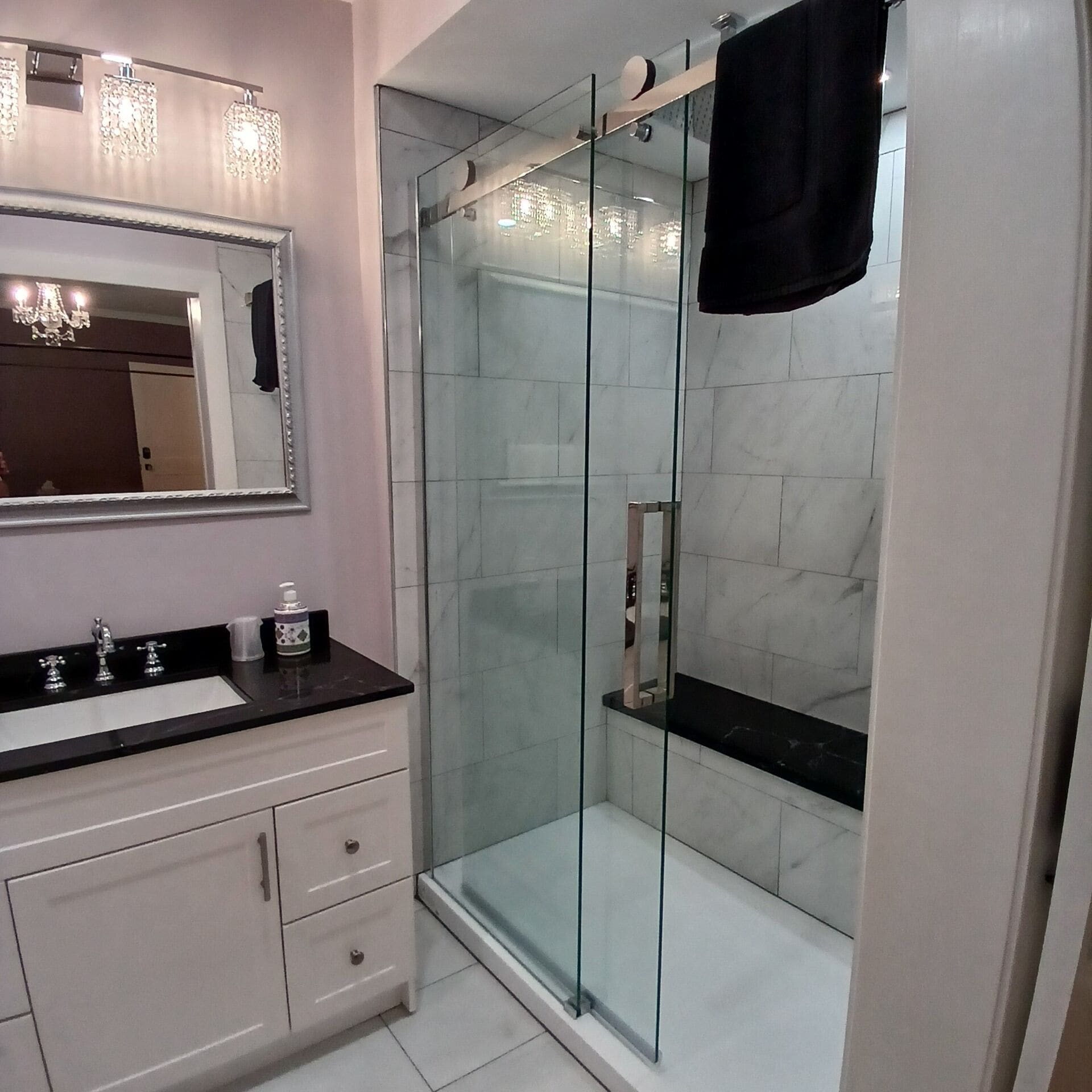 Un baño moderno con ducha de vidrio, tocador con encimera negra y un espejo grande sobre el lavabo.
