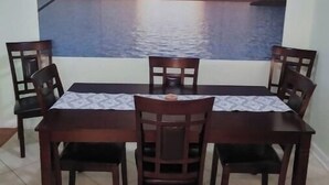 A dining area with a table and chairs, a large painting of a sunset over water, and a tiled floor. - Entire 2 bedroom home w/1 car garage in Inverness (Inverness)