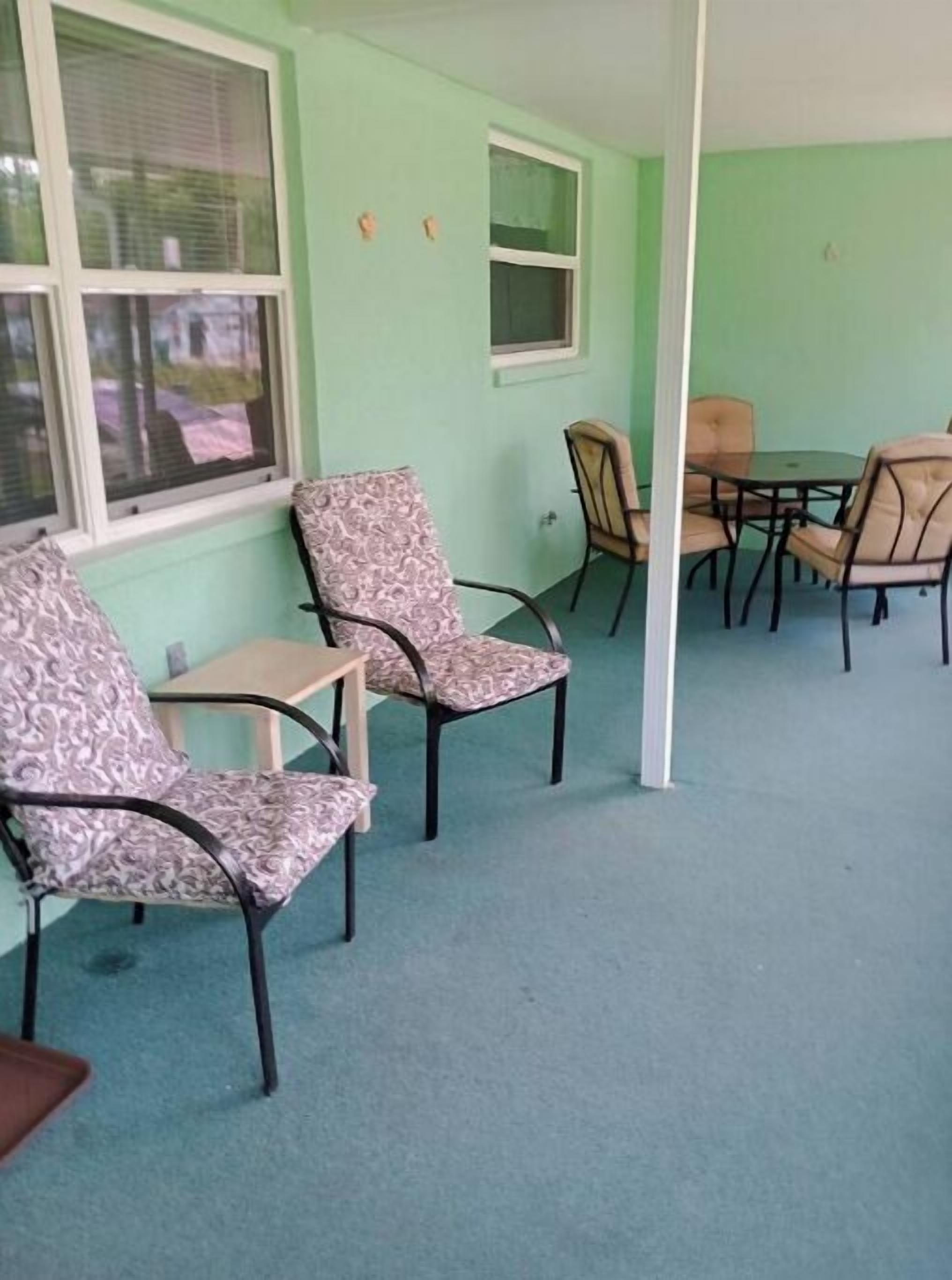 Ein Zimmer mit zwei gemusterten Sesseln, einem kleinen Tisch und einem Fenster mit Jalousien.