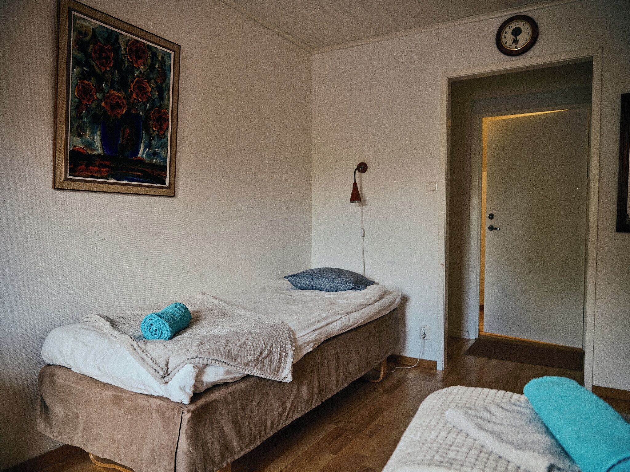 Una habitación con una cama, un cuadro, un reloj y una puerta.