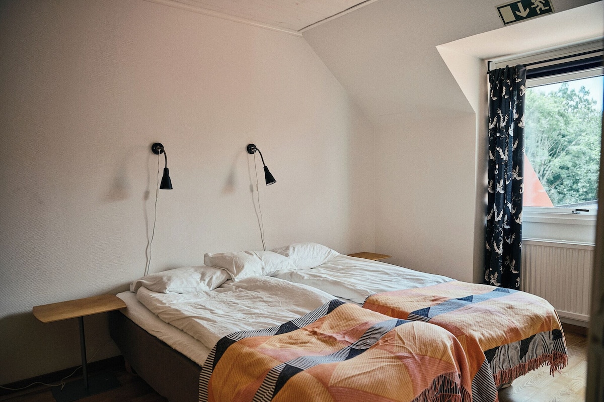 Une chambre à coucher avec un lit, deux lampes de chevet, une fenêtre avec des rideaux et une table de chevet en bois.