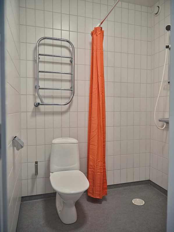 A small, tiled bathroom with a white toilet, a metal towel rack, and an orange shower curtain. - Herrestad Bed & Guestroom (Varnamo)