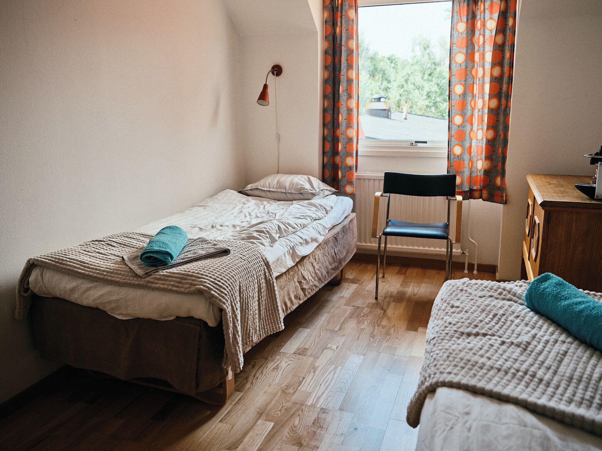 A small, tidy bedroom with a single bed, a chair, and a desk.