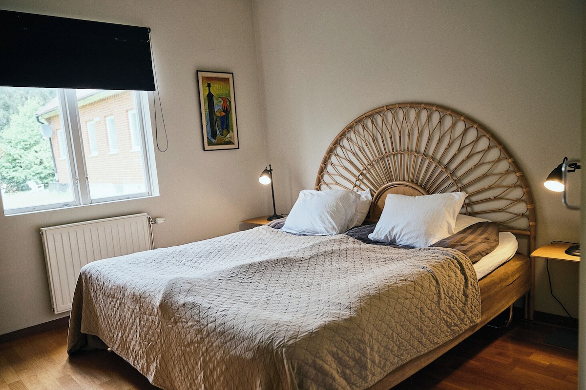 Une chambre à coucher comprenant un lit, une table de chevet, une lampe, un radiateur, une fenêtre et un tableau accroché au mur.
