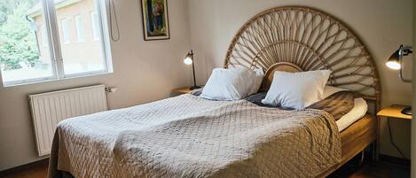 A bedroom with a bed, a bedside table, a lamp, a radiator, a window, and a painting on the wall.