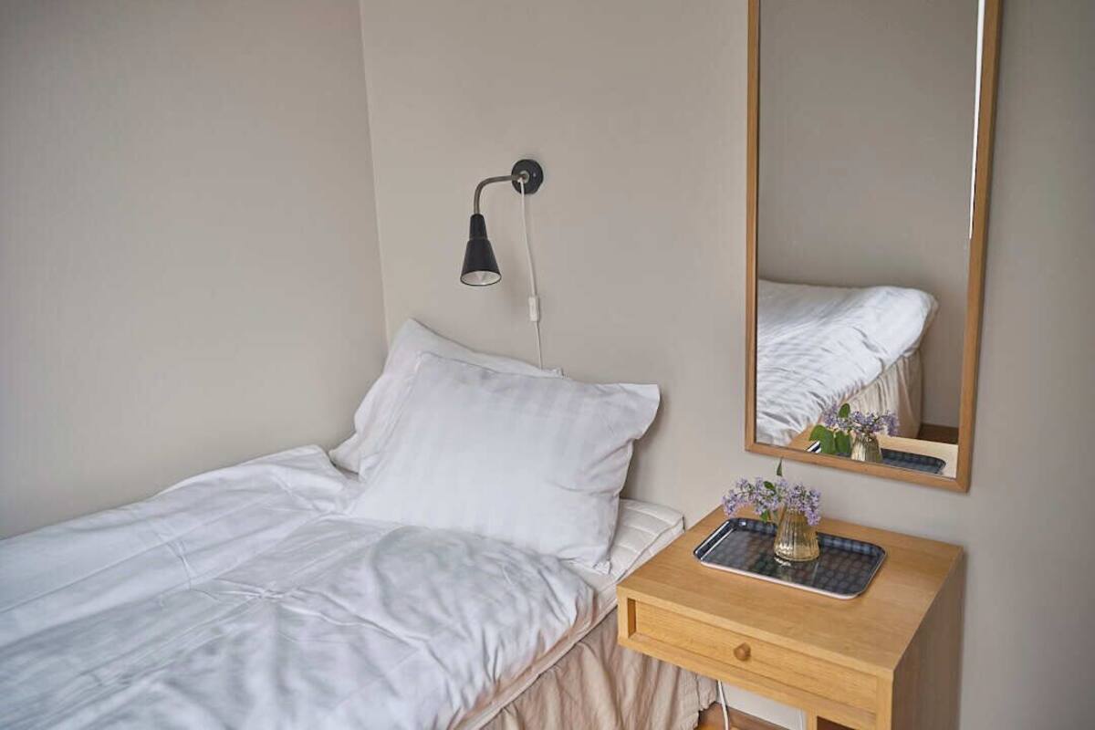 Une chambre à coucher avec un lit, une table de chevet avec une lampe, un miroir et un petit vase avec des fleurs.