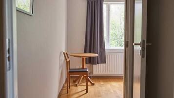 Un pasillo con suelo de madera, una mesa con una silla, una ventana con cortinas y una lámpara en el techo.