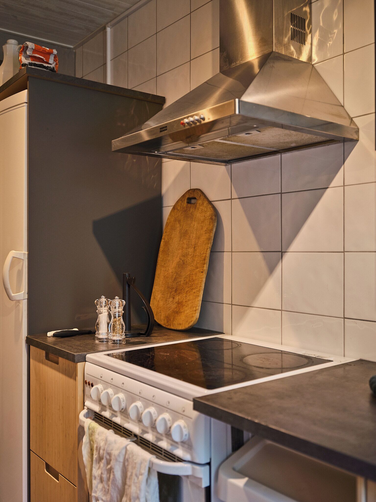 Una cocina con estufa, horno y una tabla de cortar de madera apoyada contra la pared.