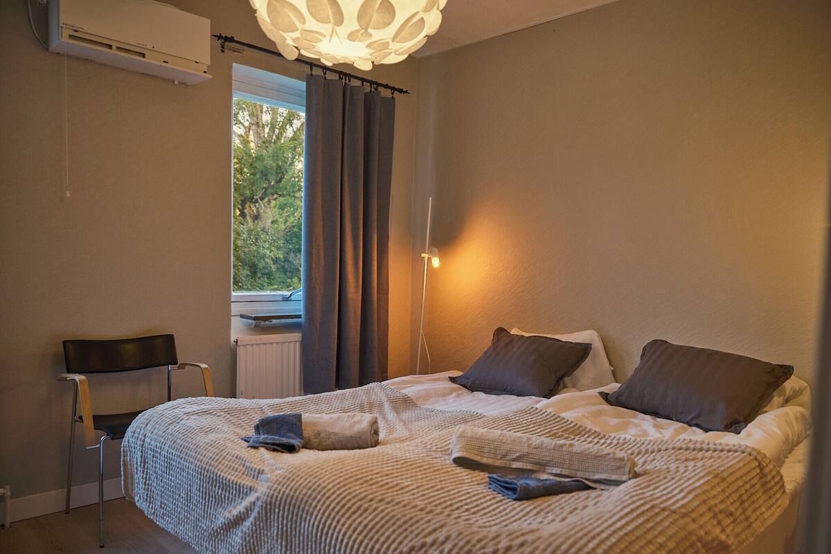 Une chambre avec un grand lit, une chaise, un radiateur et une fenêtre avec des rideaux.