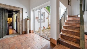 En rymlig hall med en trätrappa som leder upp till en balkong, en krukväxt och utsikt över omgivningen.