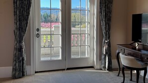 A room with a double door leading to a balcony, a television on a stand, and a chair.