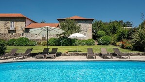 A poolside area with lounge chairs and an umbrella, surrounded by stone buildings and greenery. - Casa do Lagar (Cabeceiras de Basto)
