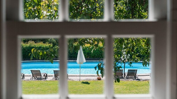 A view of a swimming pool with lounge chairs and a white umbrella, viewed through a window with a white frame. - Casa do Lagar (Cabeceiras de Basto)