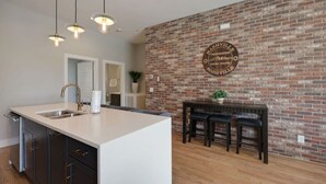 A kitchen with a large island, a brick wall with a Nashville sign, and a bar area with stools. - Spacious West End | Rooftop Skyline Retreat (Nashville)