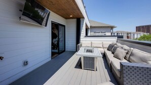 A rooftop patio with a sofa, a table, and a TV mounted on the wall. - Spacious West End | Rooftop Skyline Retreat (Nashville)