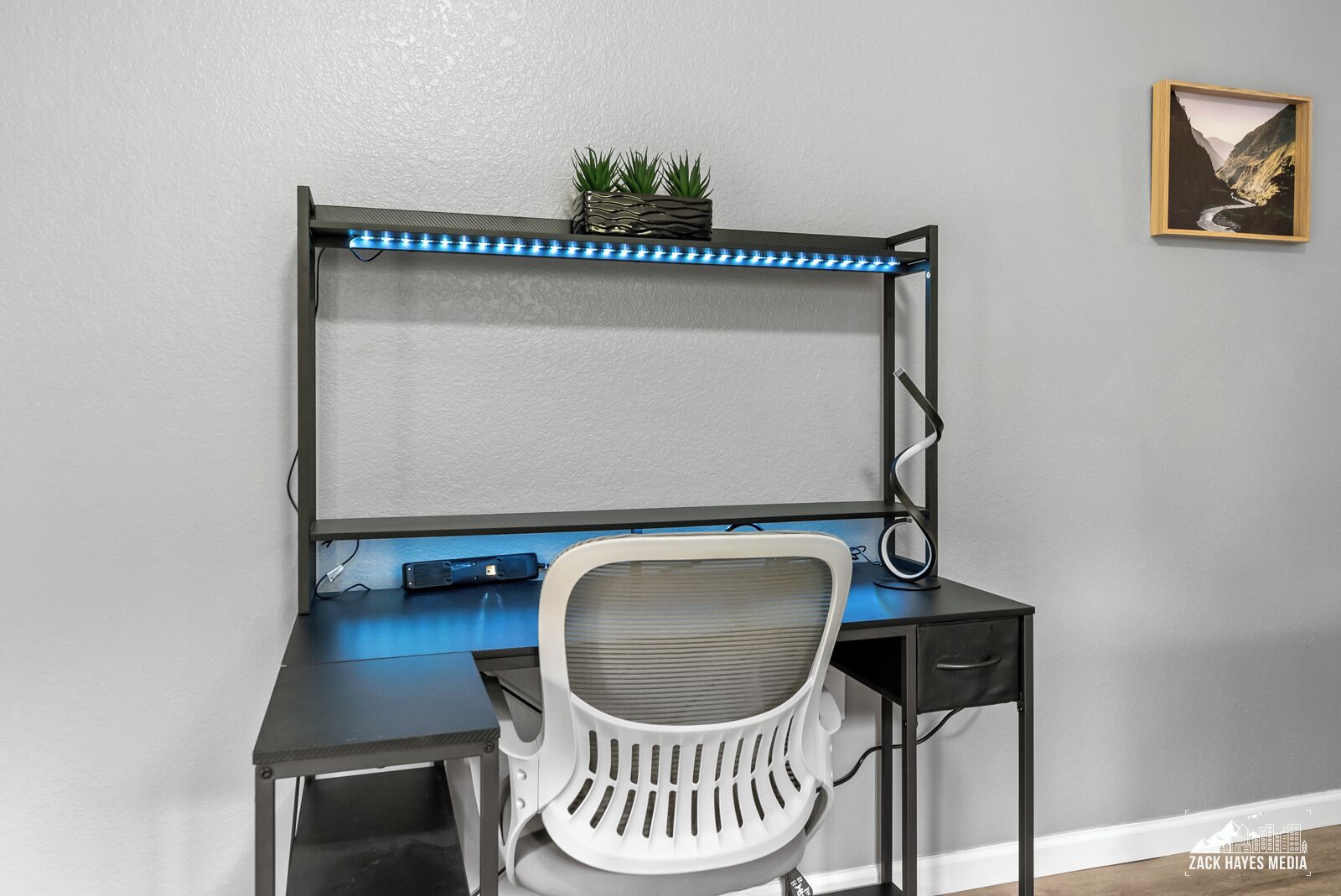 A modern desk with a computer, a chair, and a shelf with plants.