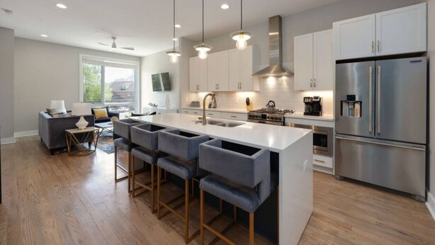 A modern kitchen with a central island, bar stools, stainless steel appliances, and pendant lighting.