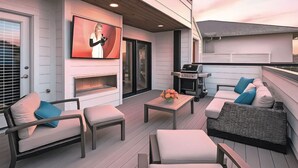 An outdoor patio with seating, a grill, and a TV screen.