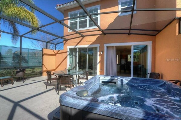 Een terras met een hottub, tuinmeubilair en een glazen ruimte.