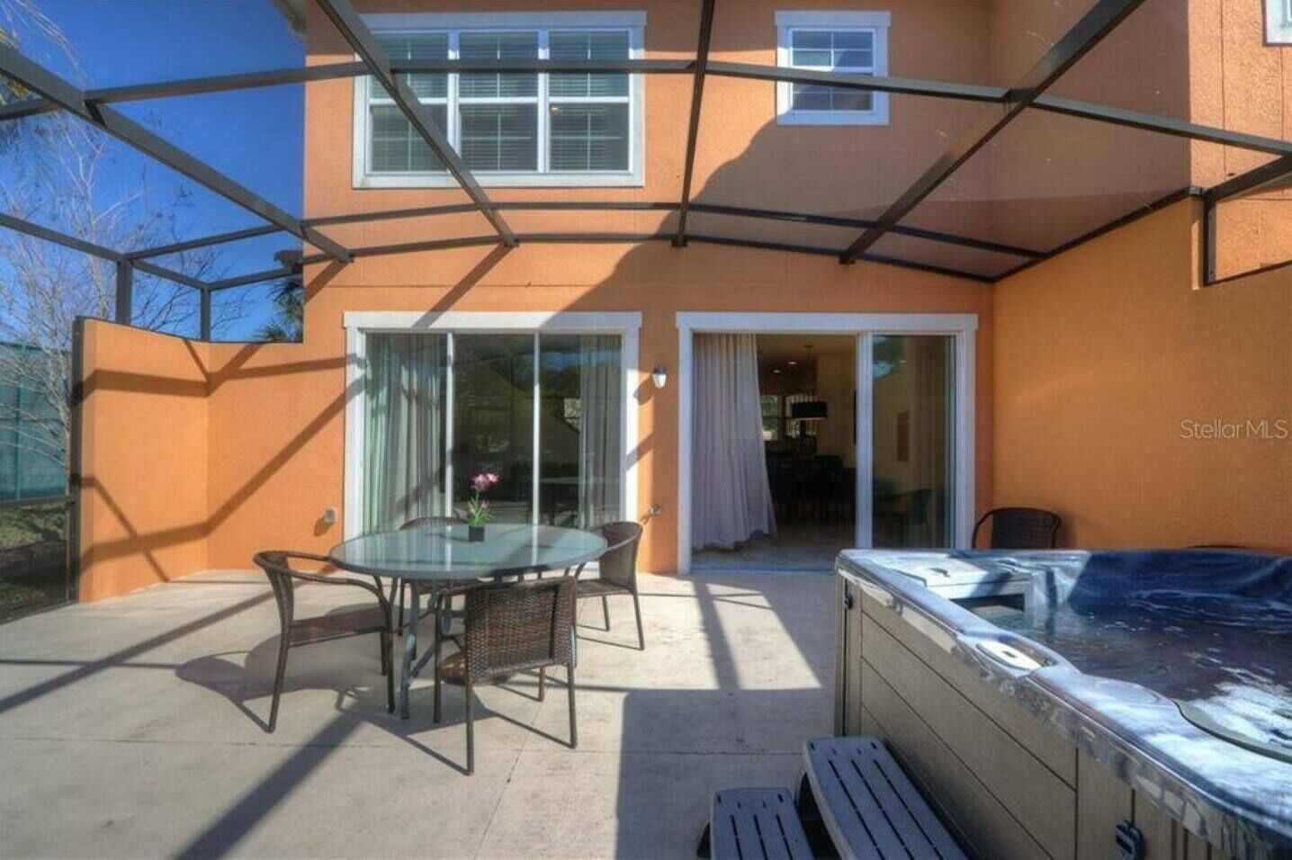 A covered patio with a glass table and chairs, a hot tub, and a sliding glass door leading to an interior space.