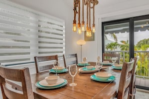 Comedor con una mesa de madera dispuesta para cuatro, persianas blancas en las ventanas y vistas al exterior.