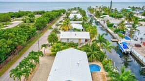 A coastal residential area with a large house featuring a swimming pool, surrounded by lush greenery and palm trees. - P61 - 2 Bed, 2 Bath with coastal chic vibe and private pool. (Marathon)