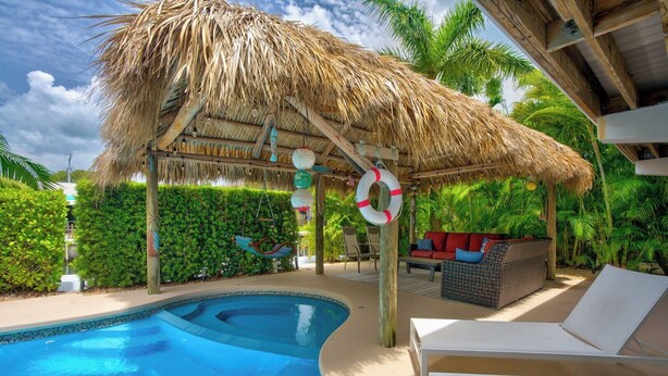A pool area with a thatched roof, lounge chairs, and a seating area with cushions. - P61 - 2 Bed, 2 Bath with coastal chic vibe and private pool. (Marathon)