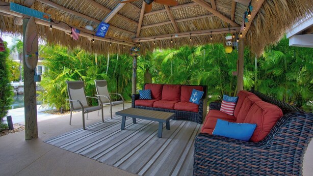 An outdoor seating area with wicker furniture, a wooden table, and a thatched roof.