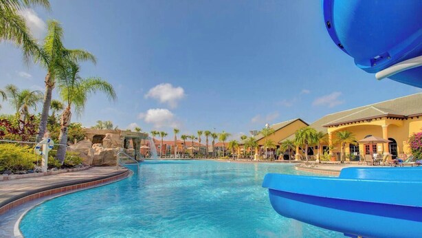 A swimming pool with a water slide, palm trees, and resort buildings in the background. - Paradise Palms 4BR | Private Pool & Themed Rooms (kissimmee)