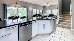 Una cocina moderna con una isla central, muebles blancos y un comedor con mesa y sillas.