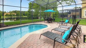 Una piscina exterior techada con sillones de descanso y una mesa, rodeada por un patio de ladrillo.