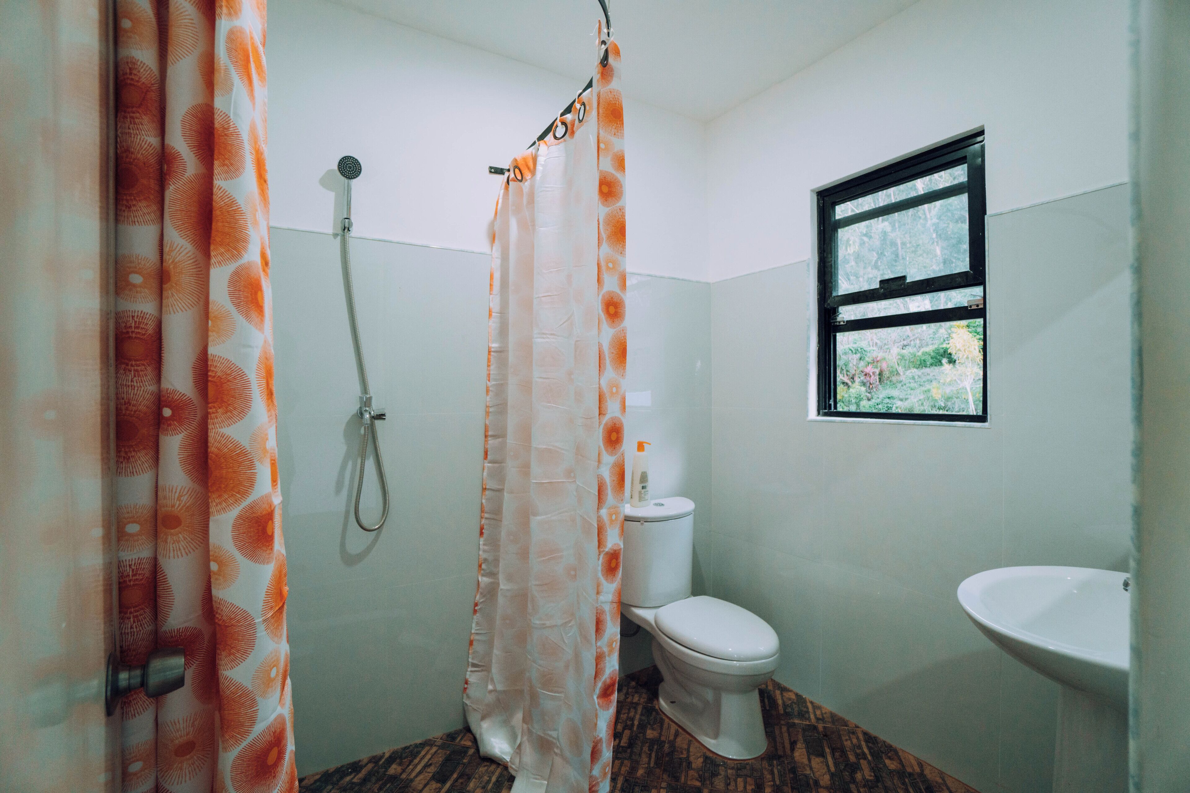 A bathroom with a shower curtain, a toilet, a window, and a sink.