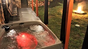 Un bain à remous éclairé d’une lumière rouge, entouré de sièges d’extérieur et d’un mur en pierre.