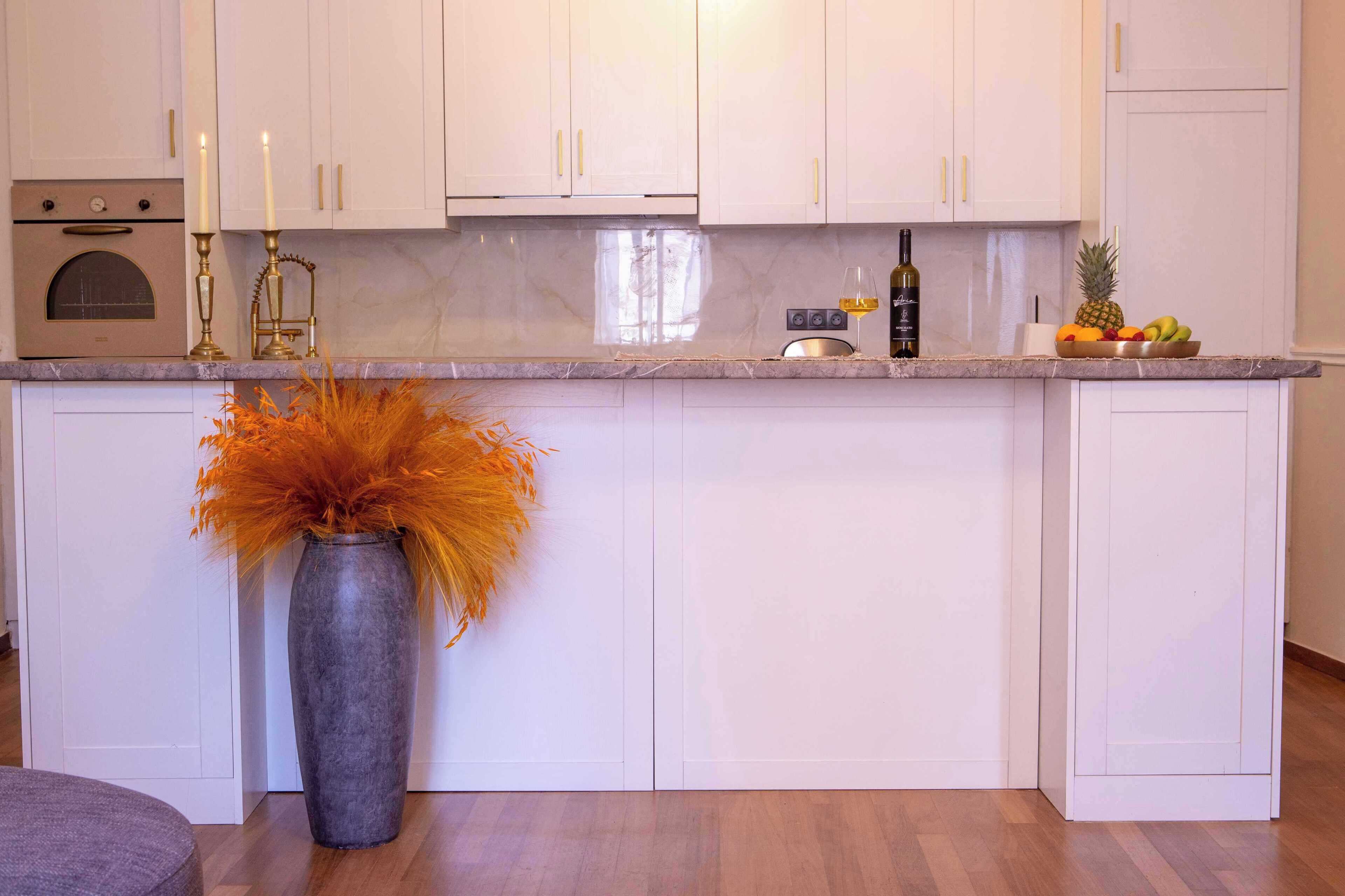 A modern kitchen with white cabinets, a marble countertop, and a vase with orange foliage.