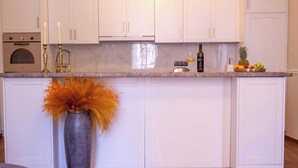 Une cuisine moderne avec des meubles blancs, un plan de travail en marbre et un vase orné de feuillage orange.