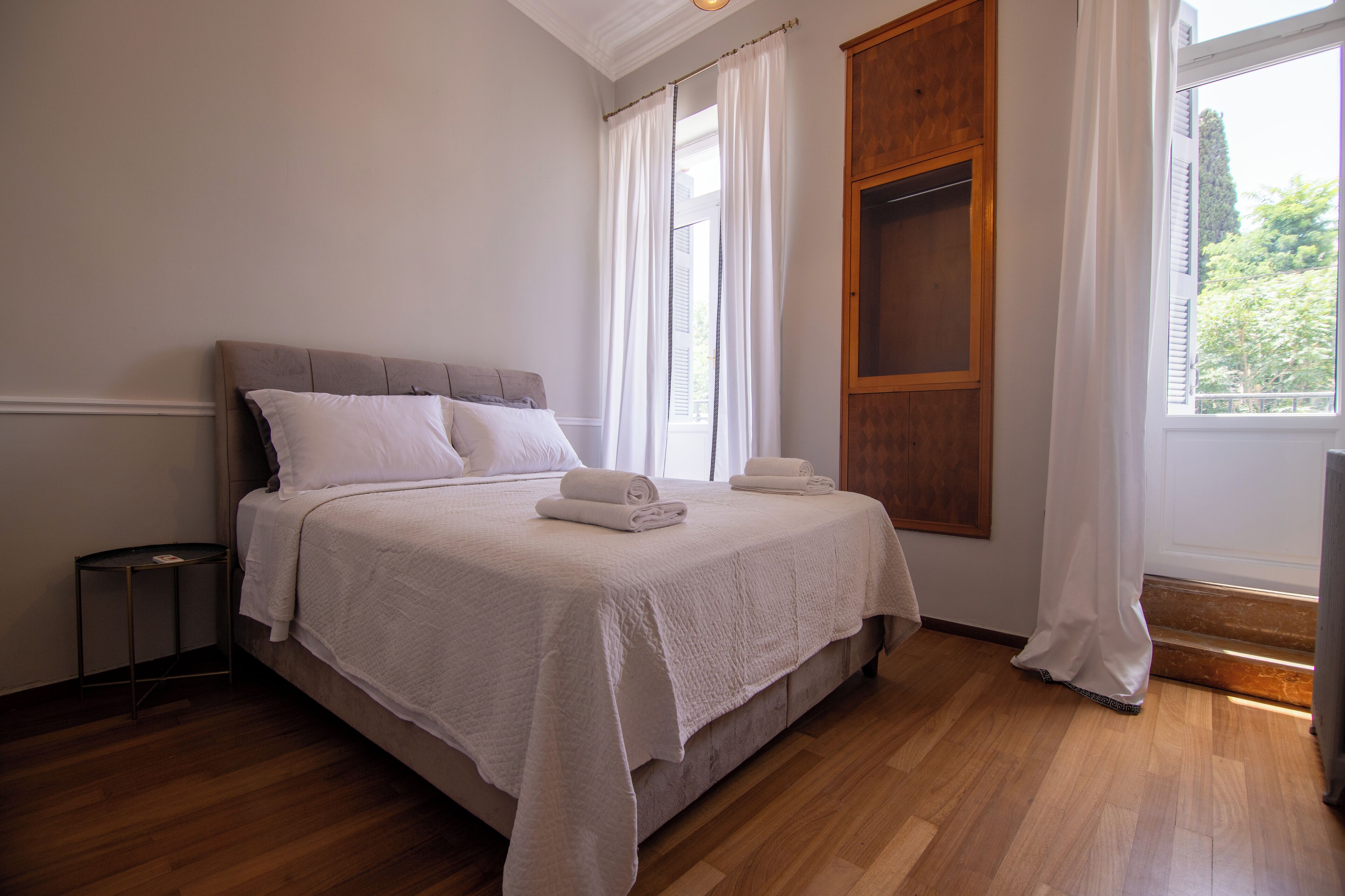A neatly made bed with white linens, a wooden headboard, and a window with curtains.