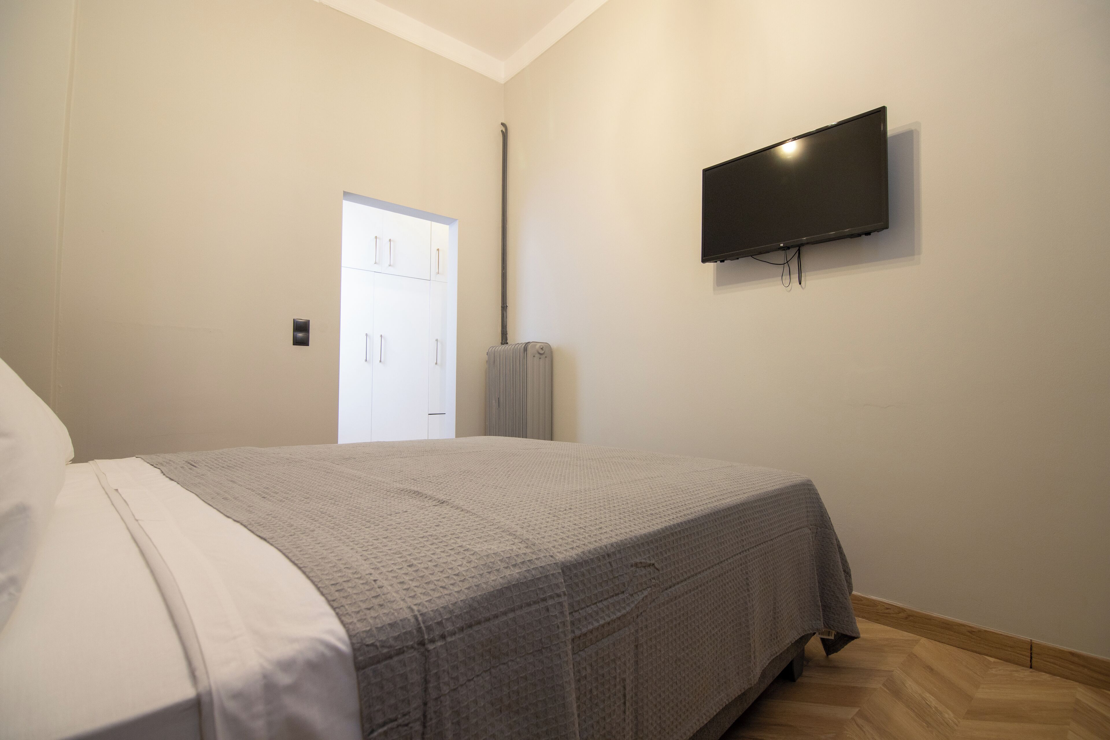 A bedroom with a bed, a television mounted on the wall, and a door leading to another room.