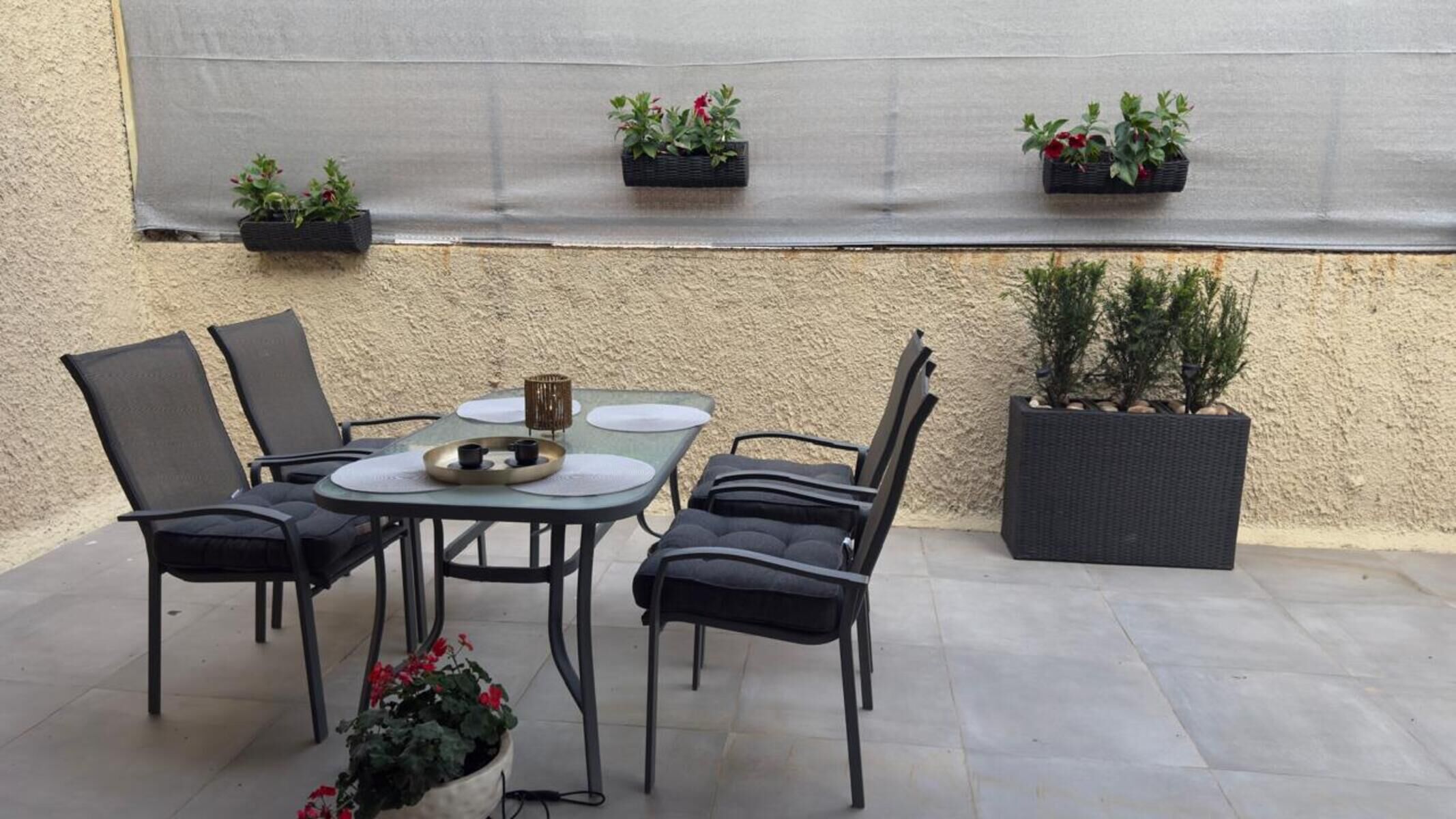 An outdoor patio with a table and chairs, potted plants, and a textured wall.