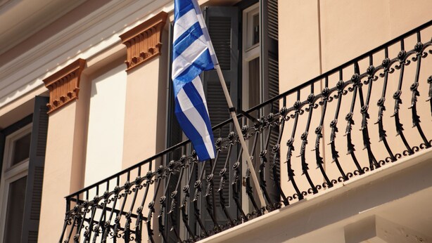 Une façade d’immeuble avec un balcon agrémenté d’une balustrade décorative et d’un drapeau.