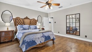 A bedroom with a large bed, wooden floor, ceiling fan, and a mirror on the wall. - The Spot at Lake Granbury (Granbury)