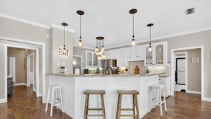A modern kitchen with white cabinets, a central island with stools, pendant lighting, and a visible 'EAT' sign. - The Spot at Lake Granbury (Granbury)